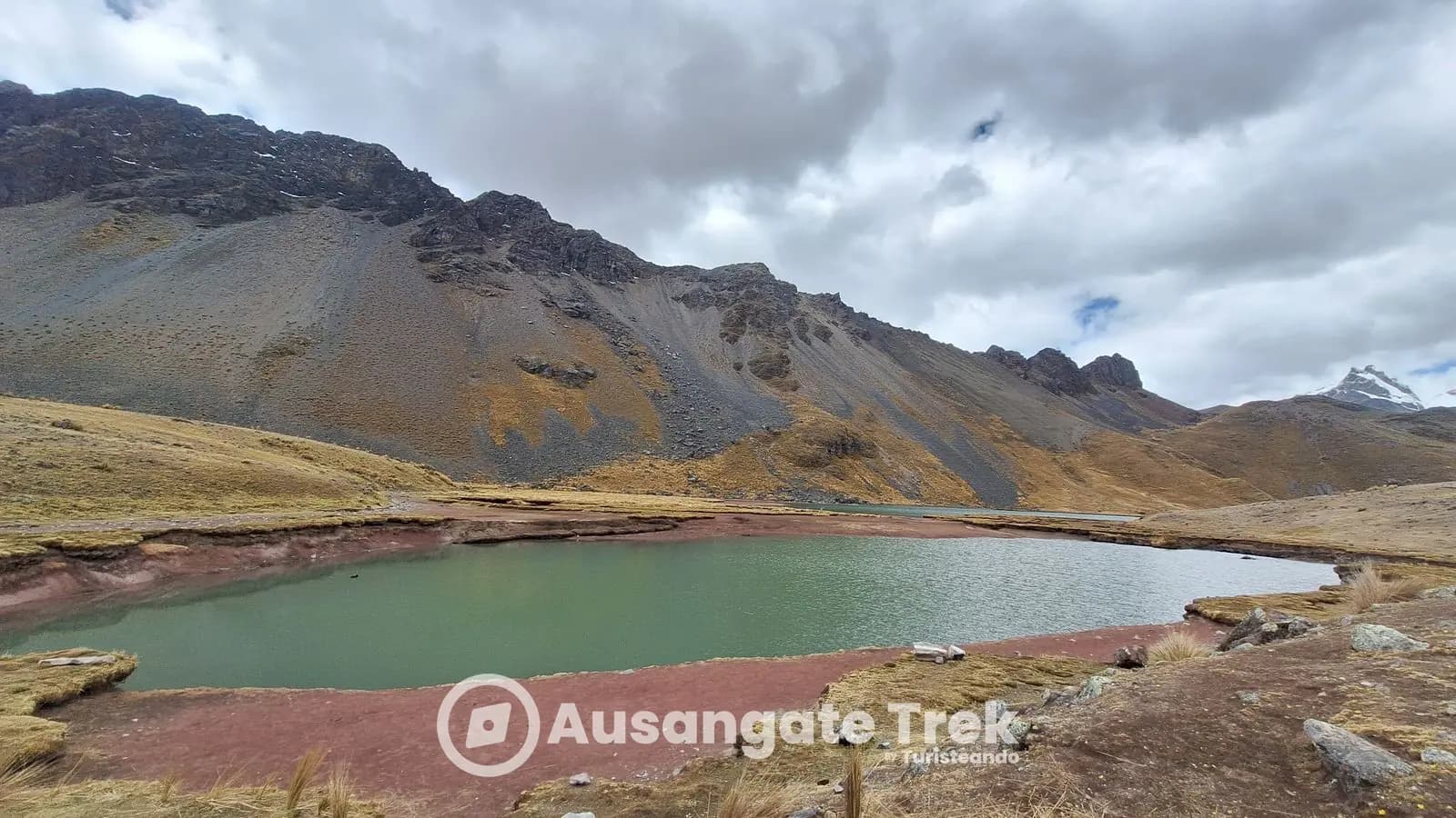 Green water ringed by red earth at Huch'uy Puka Qocha, Ausangate 7 Lakes, Peru